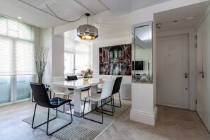 Ein stilvoller Essbereich mit einem weißen Tisch, schwarzen Stühlen, einer Hängeleuchte und einem großen gerahmten Bild an der Wand.