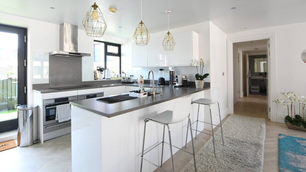 Una cocina moderna con una isla central, electrodomésticos de acero inoxidable, iluminación colgante y vistas al exterior.