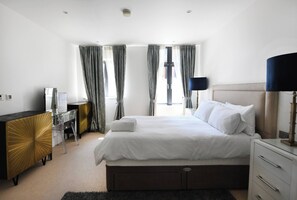 Ein Hotelzimmer mit Bett, Nachttisch, Lampe, Kommode und Schreibtisch mit Stuhl.