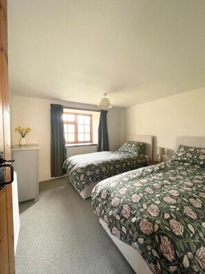 A bedroom with two beds, a window with curtains, a bedside lamp, and a small cabinet. - The Longhouse at Pencwm Escapes (Hebron)