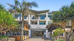 A multi-story hotel with a modern architectural design, featuring a prominent entrance with a covered walkway and palm trees. - Sandy Toes Paradise at Paradiso 111 (Kingscliff)