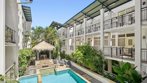 A pool area with a thatched gazebo, lounge chairs, and a multi-story building with balconies. - Sandy Toes Paradise at Paradiso 111 (Kingscliff)