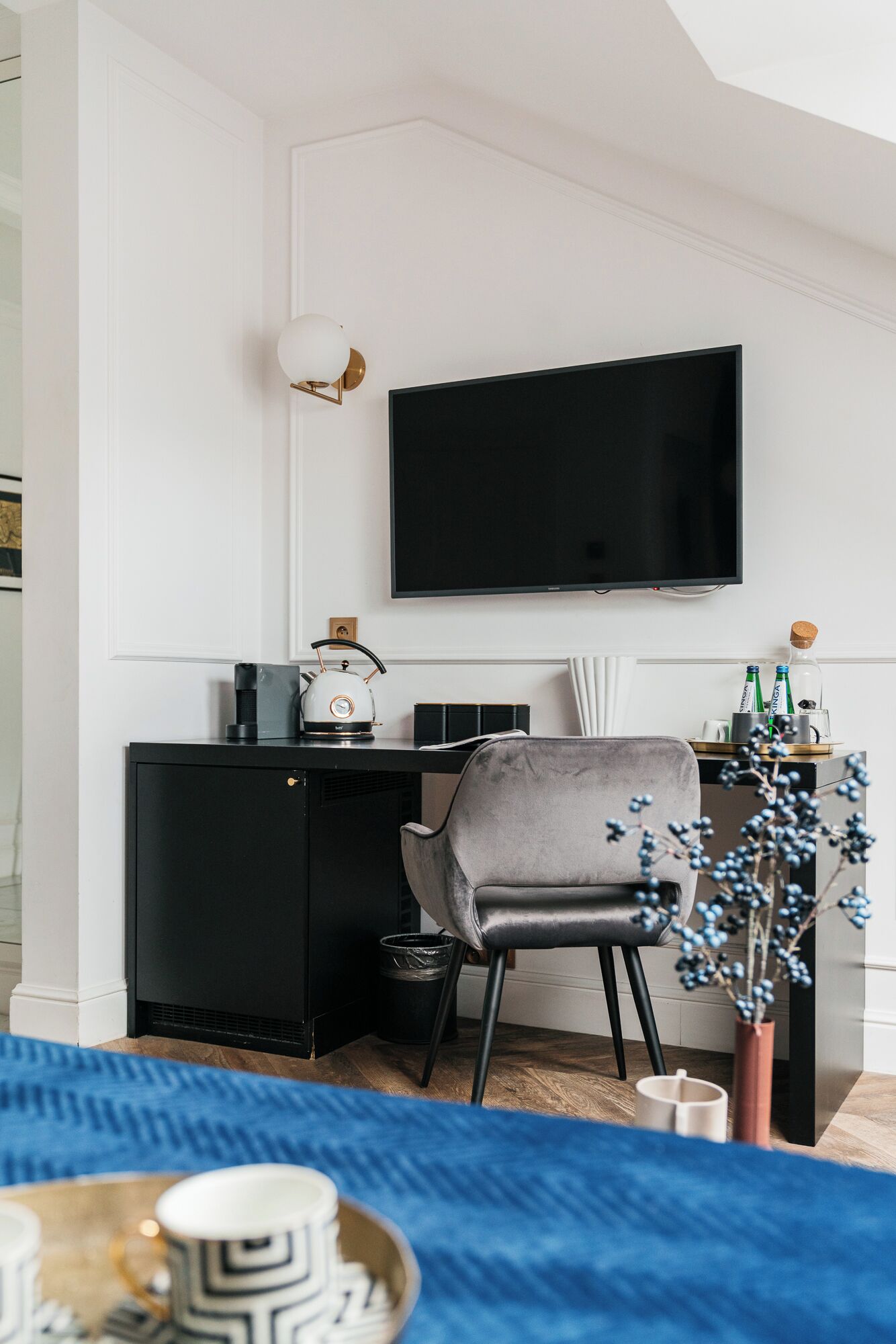 Un salon moderne avec une télévision noire, un fauteuil gris, une petite table avec une bouilloire et un tapis bleu.