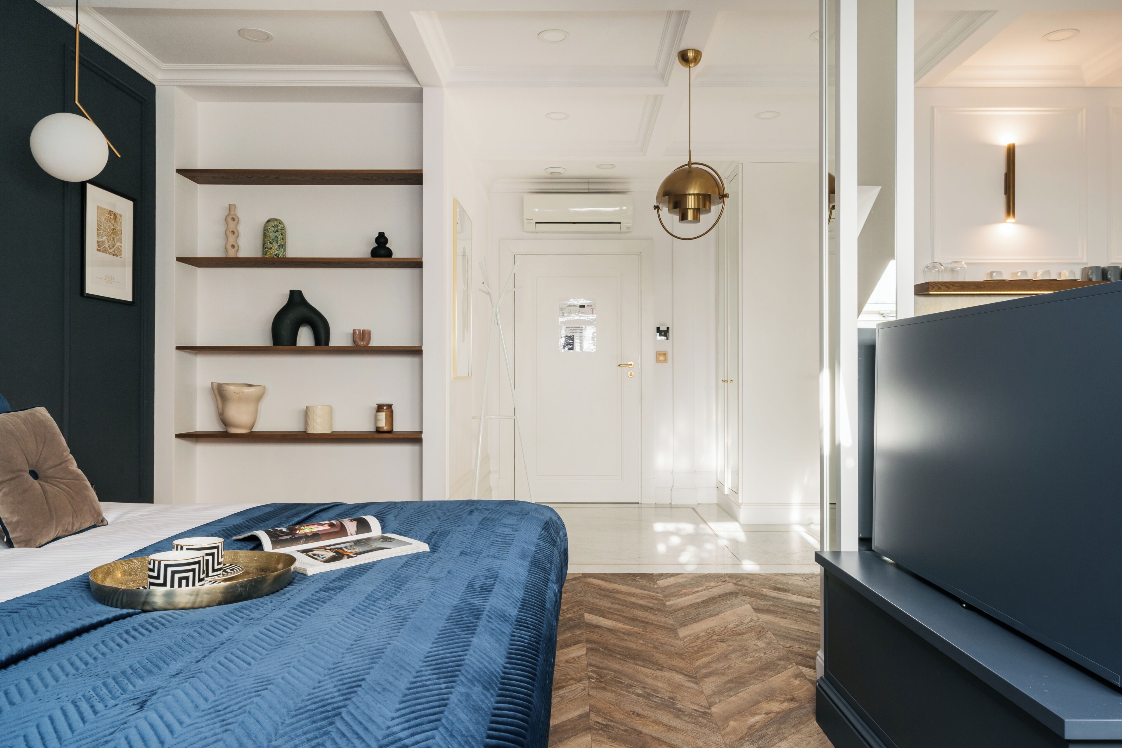 A modern hotel room with a large bed, a flat-screen TV, and a wooden herringbone floor.