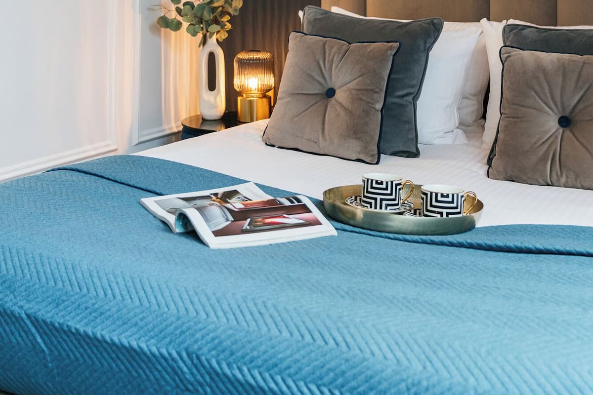 A modern bedroom with a bed, bedside lamps, a framed picture, and a magazine on the bed.