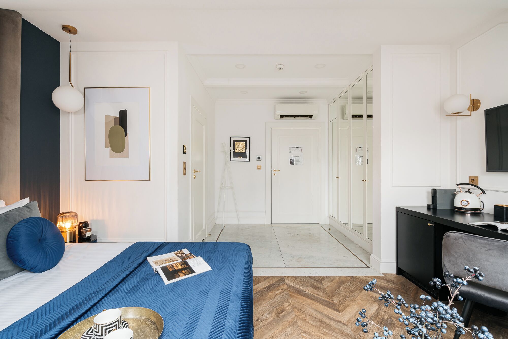 A modern bedroom with a bed, bedside table, lamp, and a view into a hallway leading to a closet.