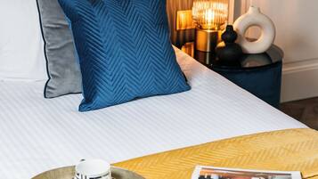 A neatly made bed with pillows, a bedside table with a lamp, and a tray with cups and saucers.