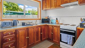 Una cocina con armarios de madera, estufa, microondas y ventana con vista a la vegetación.