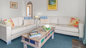 Un salón con un sofá blanco, una mesita de centro con un libro y un cuadro enmarcado de Tasmania.