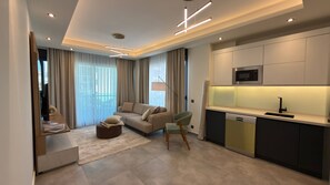 A modern living room with a sofa, a dining area with a kitchen, and a balcony with curtains. - 2-bedroom apartment in lovely Alanya with AC and fitness room (Alanya)