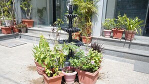 Un patio con plantas en macetas, una fuente y escalones que conducen a la entrada de un edificio.