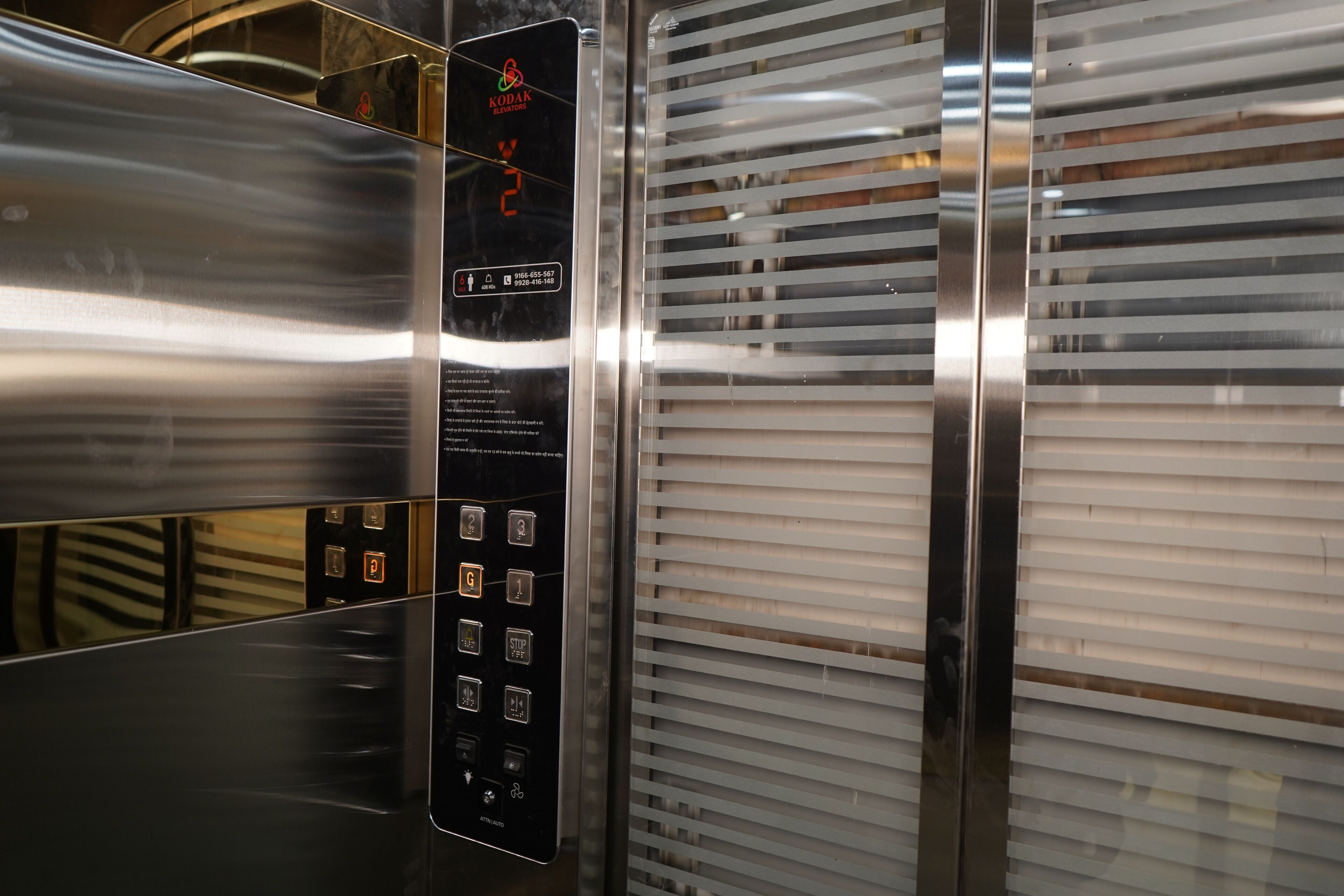An elevator interior with metallic walls, a control panel with buttons, and horizontal blinds.