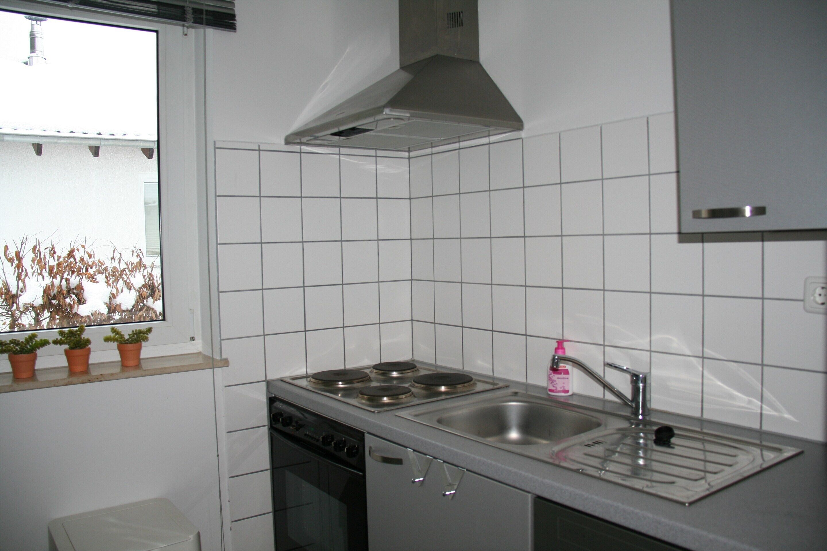 Eine Küche mit Herd, Spüle und Fenster mit Blumentöpfen.