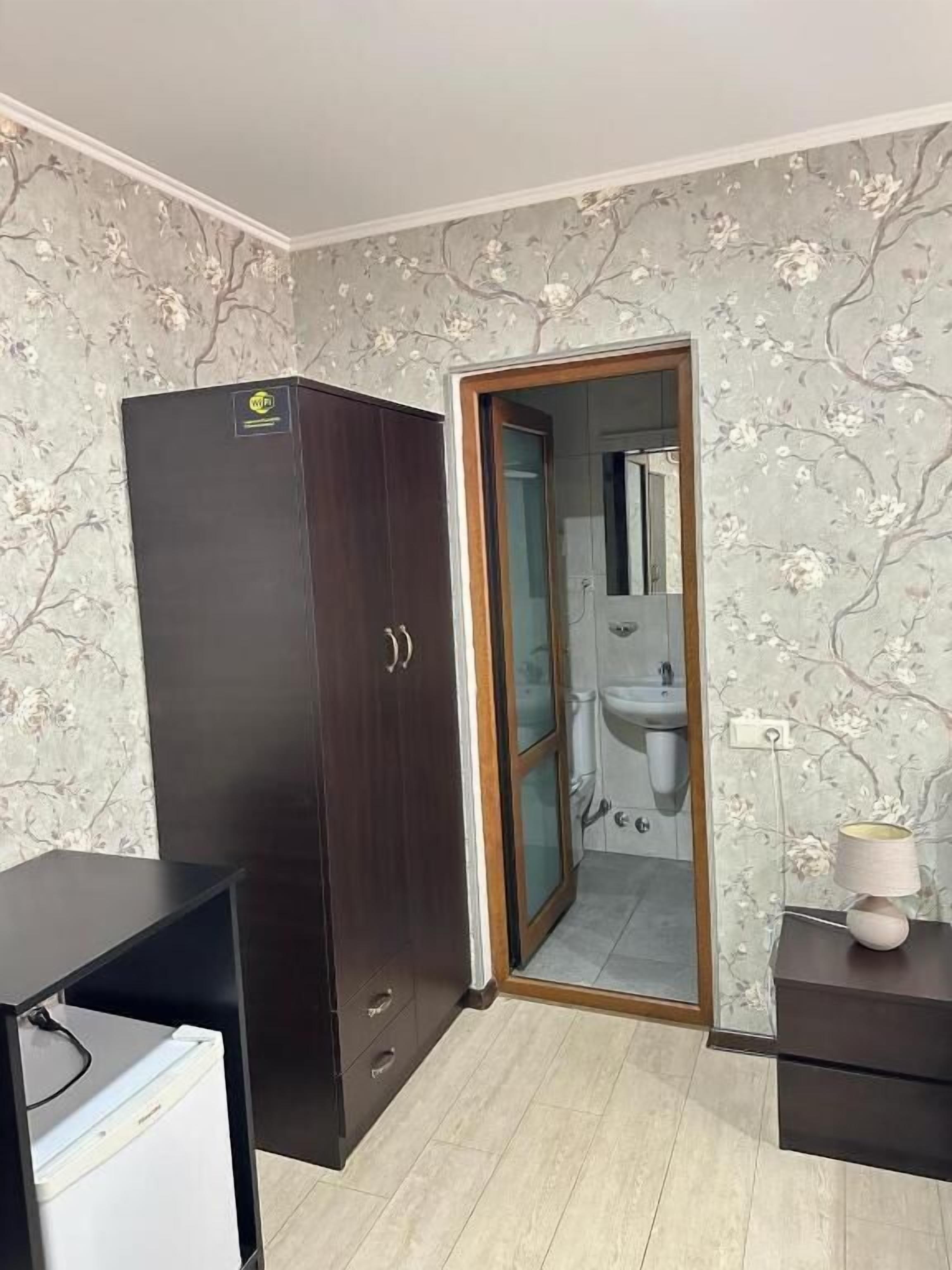 A room with a wardrobe, a desk with a lamp, and a bathroom visible through an open door.