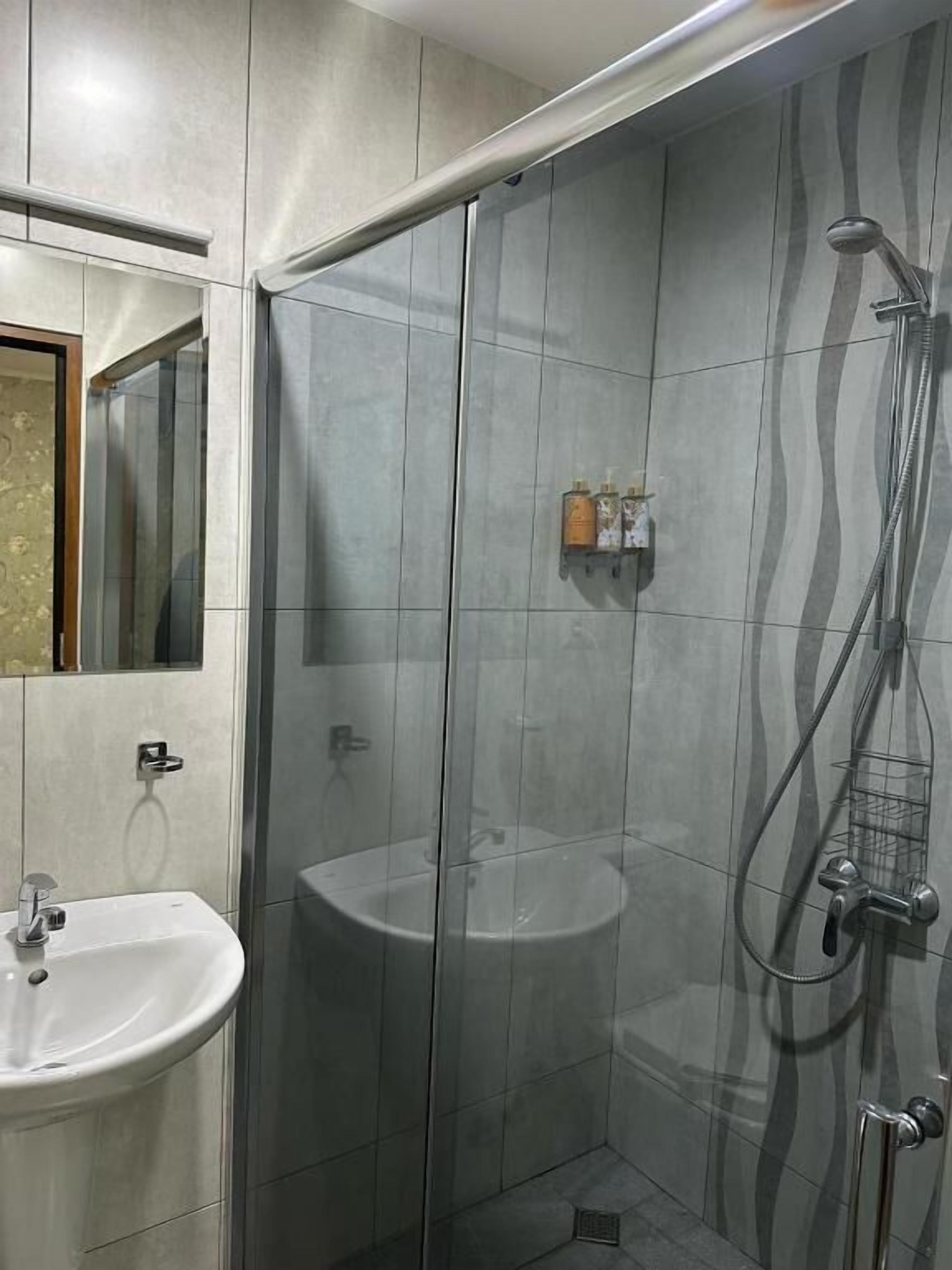 A bathroom with a glass shower enclosure, a sink, and a mirror.
