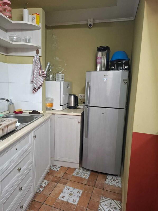 A compact kitchen with white cabinets, a stainless steel refrigerator, a coffee maker, and a kettle on the countertop. - Hotel Nebula Plaza  (Tbilisi)