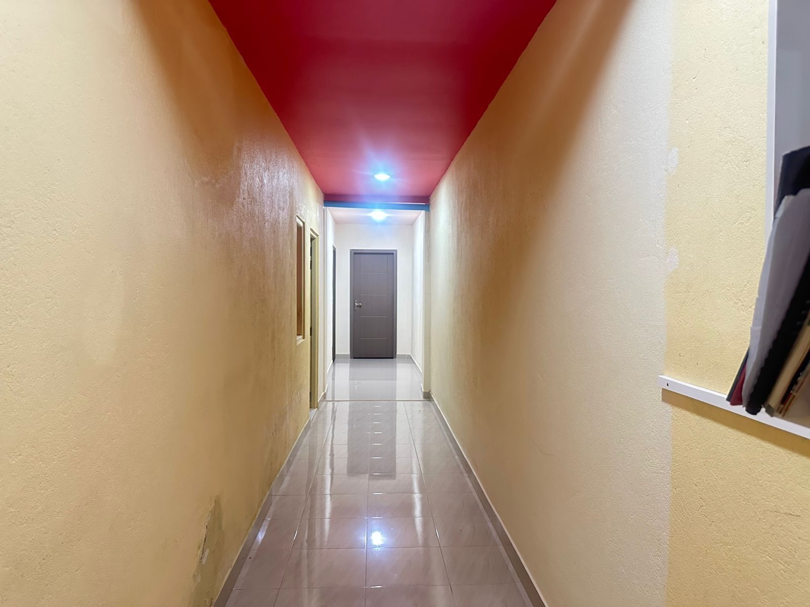 Passadís estret amb sostre vermell, una porta al final i una làmpada penjant a dalt.