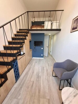 A modern interior with a wooden staircase, a blue accent wall, a flat-screen TV, and a gray armchair. - Nebula Boutique Hotel (Tbilisi)