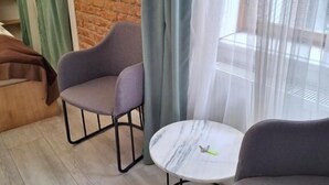 Ein Zimmer mit einer Backsteinwand, einem runden Tisch, zwei Sesseln und einem Fenster mit transparenten Vorhängen.