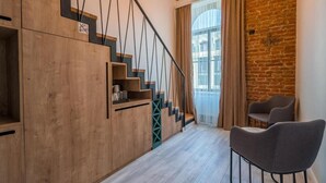 Eine Treppe mit Holzbeschlägen und schwarzen Geländern, ein Fenster mit Vorhängen sowie zwei graue Stühle.