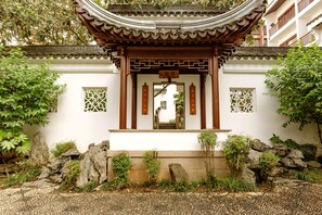 Un portón chino tradicional con diseños intrincados, rodeado de un jardín con rocas y plantas.