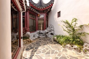 A traditional courtyard with stone flooring, a red wooden door, and a small rock formation. - Wu Palace Hotel Suzhou (Suzhou)