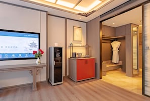 A hotel room with a TV displaying a weather forecast, a red minibar, a small table with a vase of flowers, and a walk-in closet with a robe. - Wu Palace Hotel Suzhou (Suzhou)