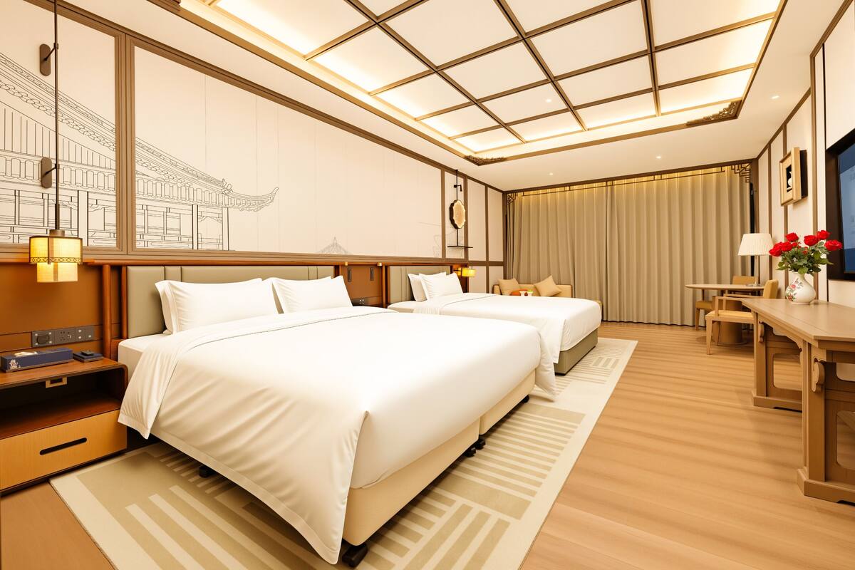 A hotel room with two beds, a desk, a chair, a lamp, and a large window with curtains.