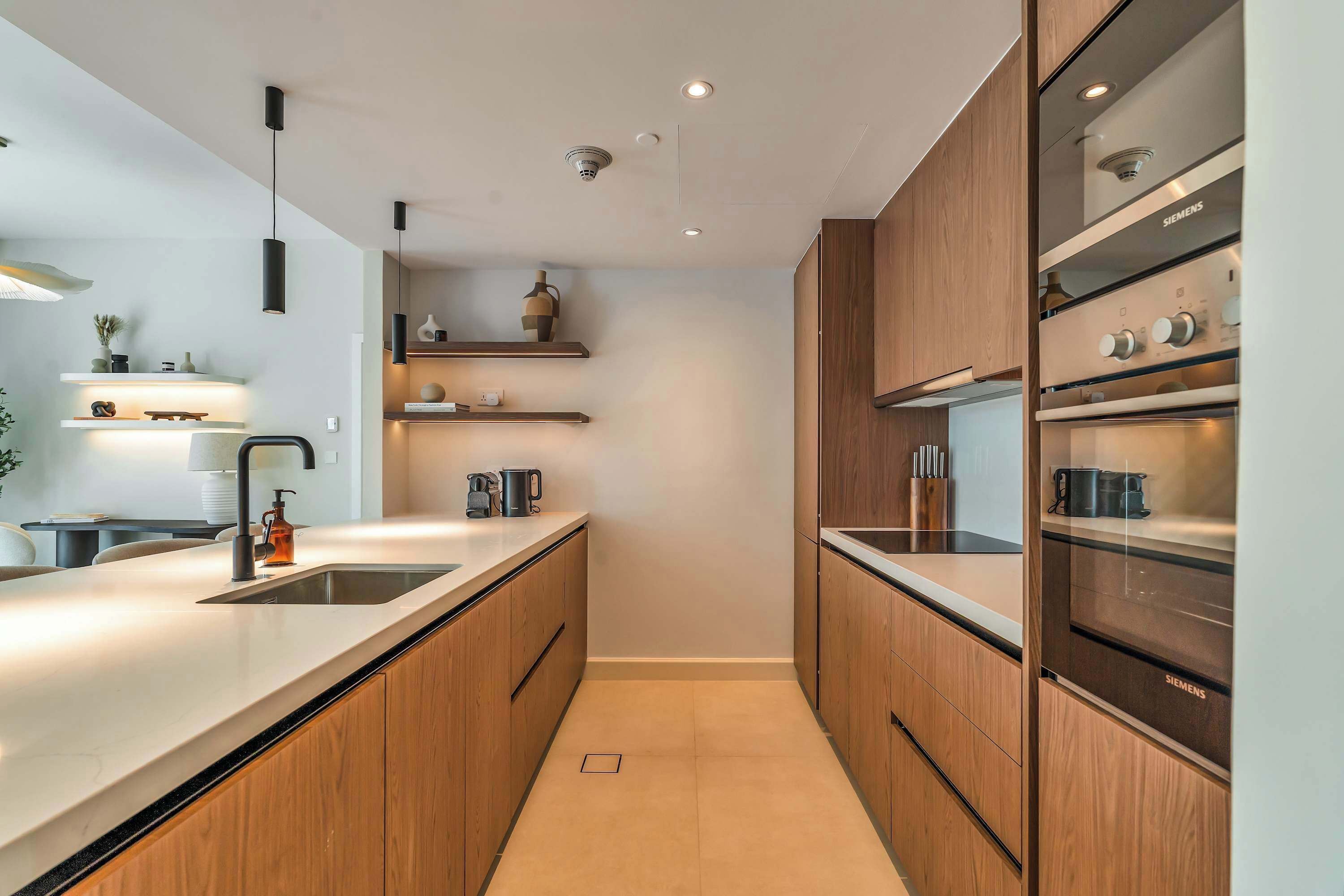 Een moderne keuken met houten kastjes, een inbouwoven en hangende lampen.