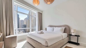 Ett modernt hotellrum med en stor säng, ett sidobord, en lampa och utsikt över stadsbilden genom stora fönster.