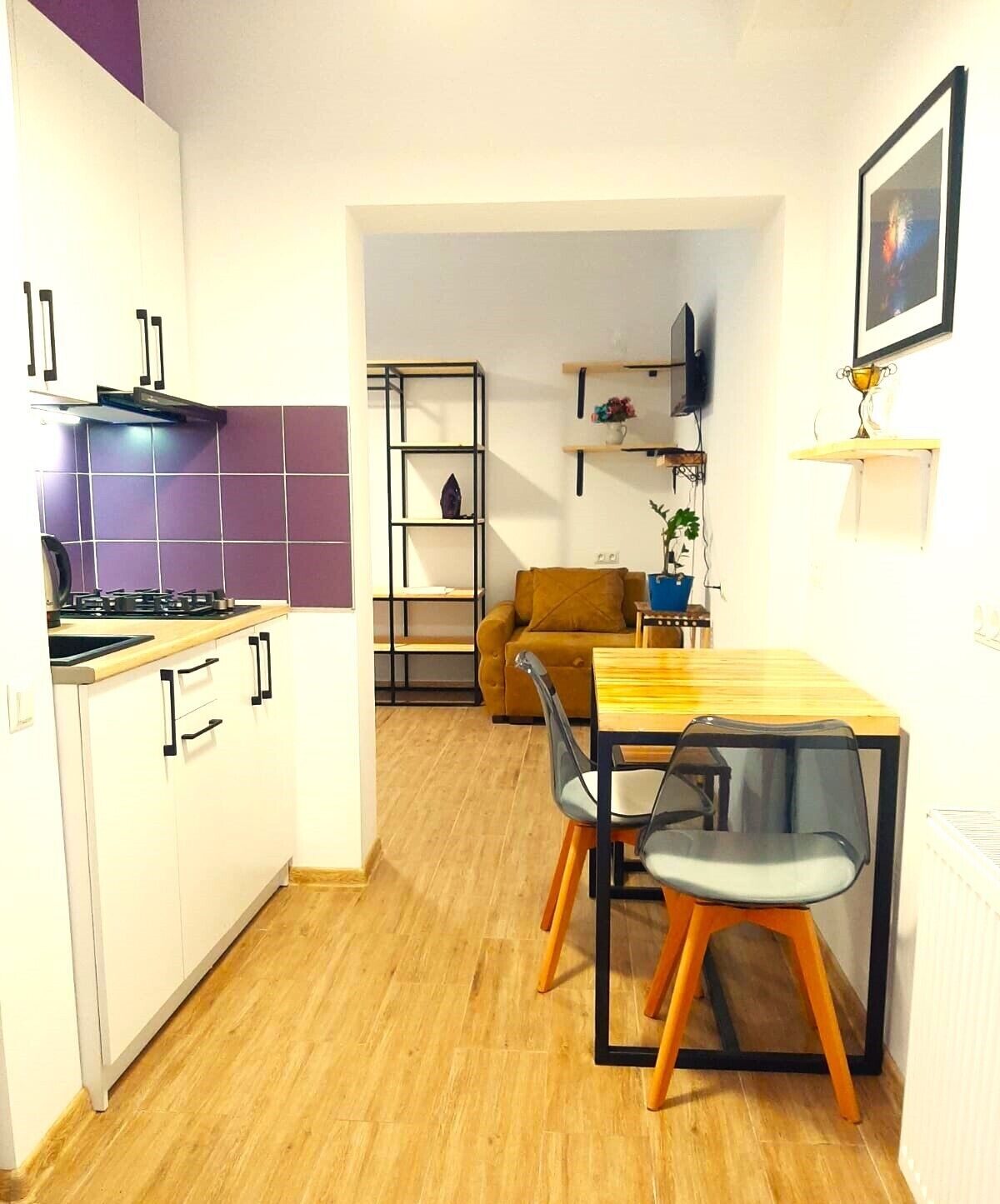 A compact kitchen with a dining area, a sofa, and a TV mounted on the wall.