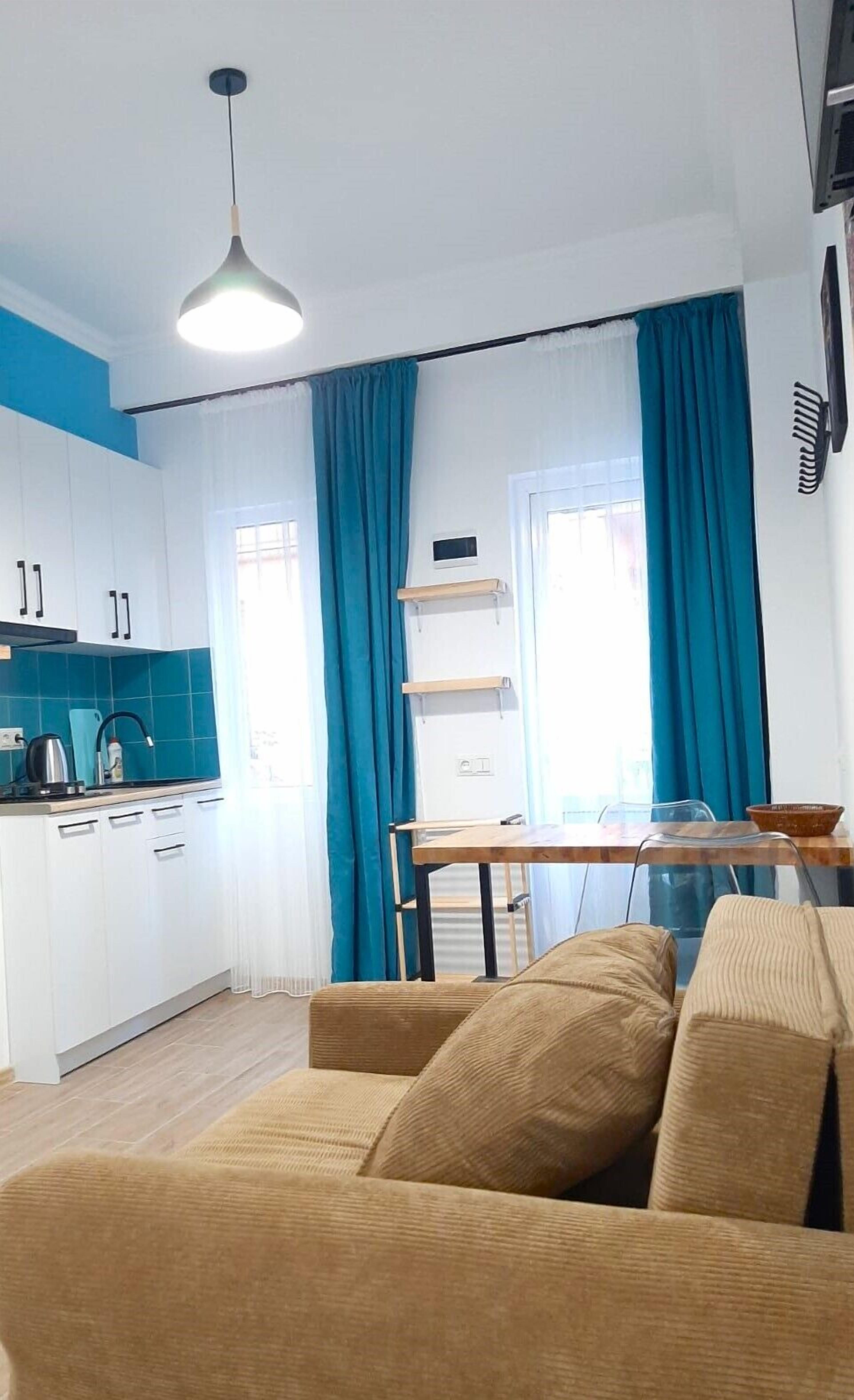 Une cuisine moderne avec des meubles blancs, un mur d’accent bleu, un coin repas doté d’une table en bois et un canapé beige.