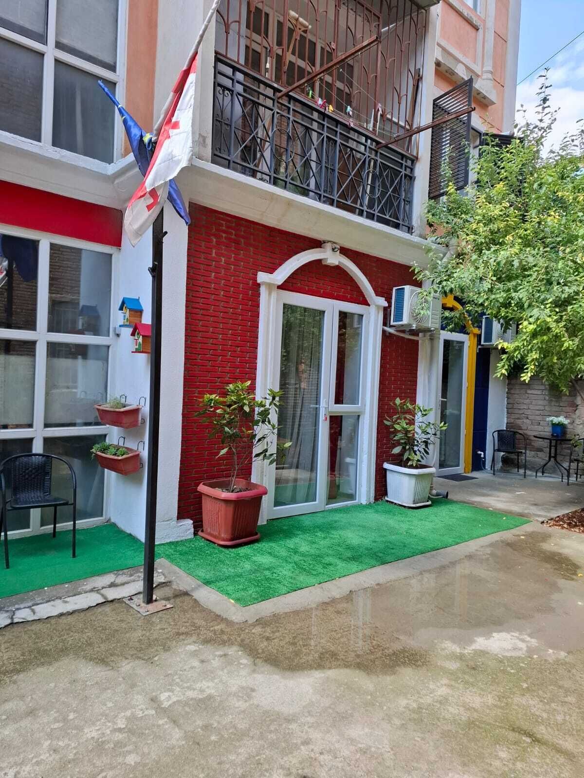 Edificio de ladrillo rojo con una puerta blanca, plantas en macetas y una bandera.