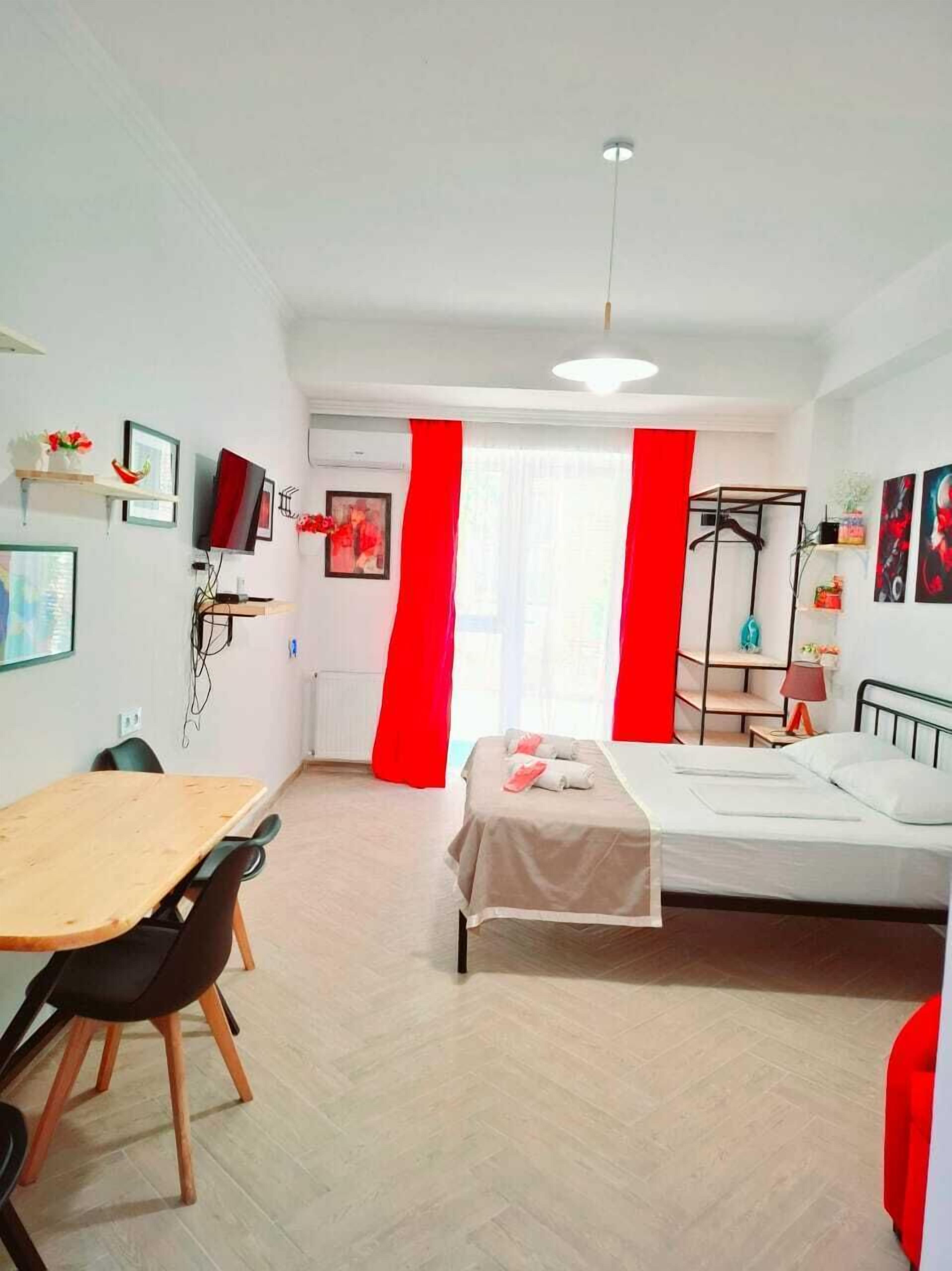 A hotel room with a bed, a desk, a chair, a TV, and a window with red curtains.