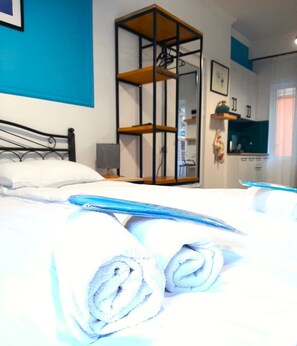 A hotel room with a bed, a wooden shelf unit, a desk, and a kitchenette. - Hotel Art Nebula (Tbilisi)