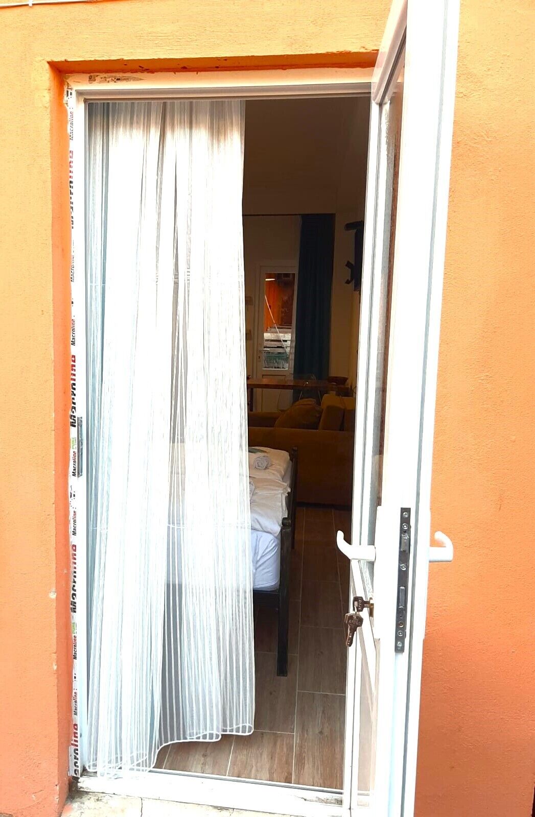 An open door to a room with a bed, a blue curtain, and a poster on the wall.