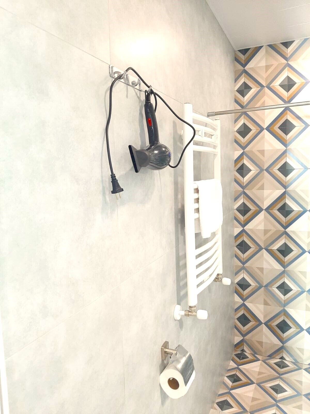 Casa de banho com porta-toalhas, secador de cabelo e suporte para rolo de papel higiénico.