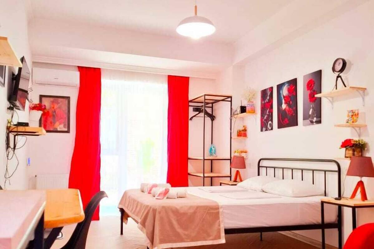 A room with a bed, a desk, a chair, a red curtain, and a wall with framed pictures.
