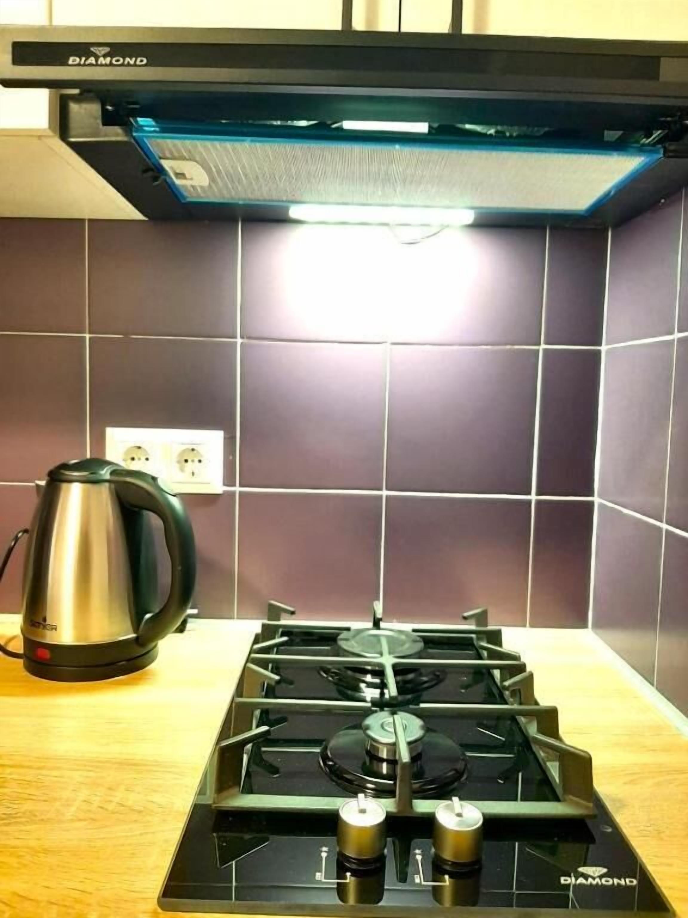 A kitchen with a gas stove, a kettle, and a wall-mounted light fixture.