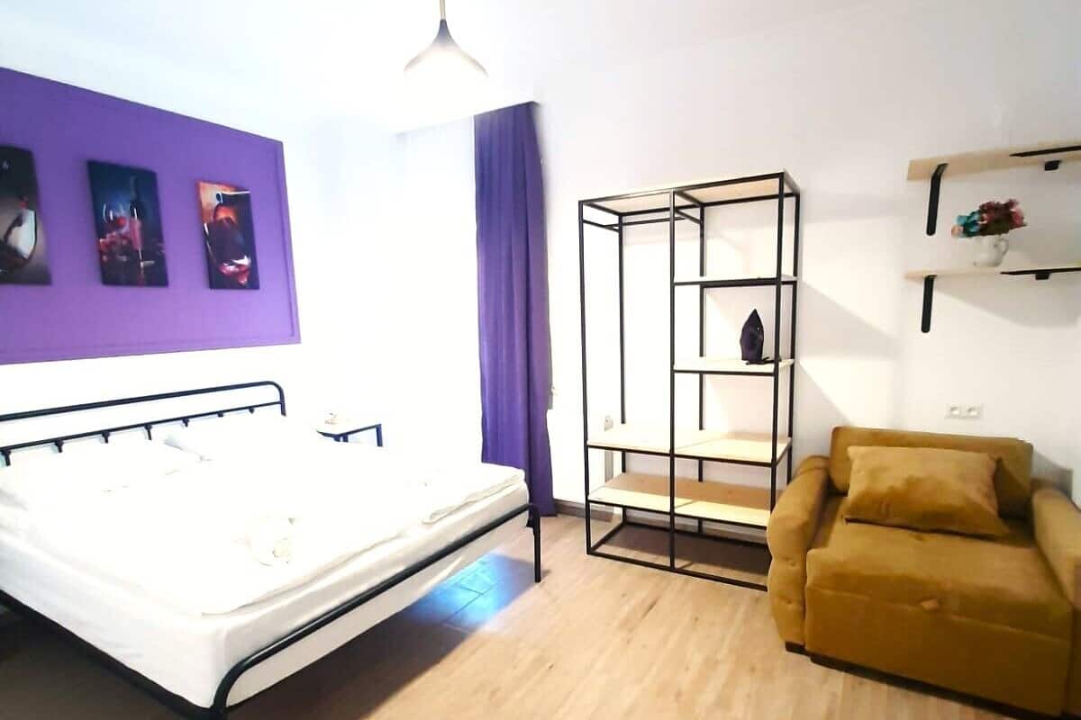 A room with a bed, a sofa, a metal shelving unit, and a wall with pictures.