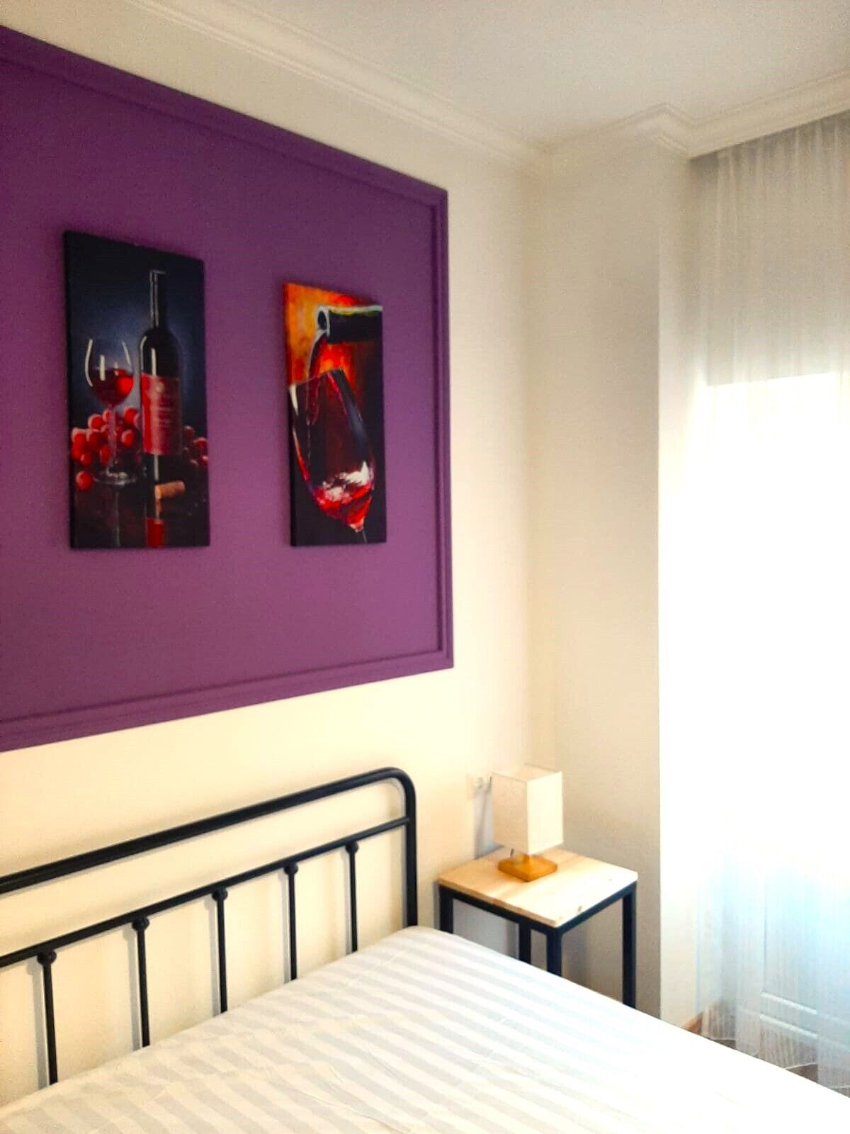 Quarto de hotel com cama, mesa de cabeceira, abajur e duas pinturas na parede.