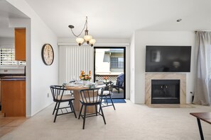 A dining area with a round table and chairs, a chandelier, a fireplace, and a TV mounted on the wall.