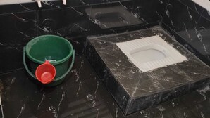 A bathroom with black marble tiles, a green bucket, a red cup, and a white toilet. - Kaku's Krishnabagh palace (Raipur Karchuliyan)
