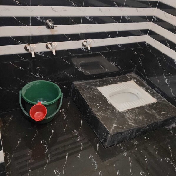 A bathroom with black marble tiles, a green bucket, a red cup, and a white toilet. - Kaku's Krishnabagh palace (Raipur Karchuliyan)