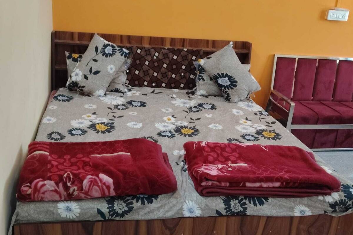 A bed with a floral bedspread, two red throw blankets, and a wooden headboard.