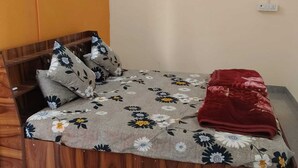 A single bed with a floral bedspread, two pillows with a floral pattern, and a red blanket. - Kaku's Krishnabagh palace (Raipur Karchuliyan)