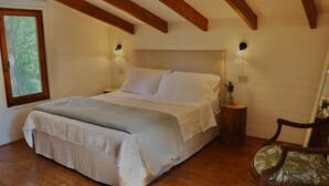 Een slaapkamer met een bed, houten balken, een nachtkastje, een stoel en een raam.