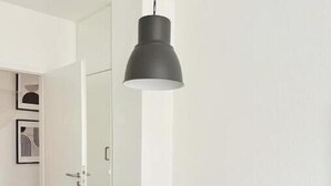 Een eetruimte met een ronde houten tafel, witte stoelen en een zwarte hanglamp.