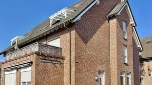 Een tweelaags bakstenen gebouw met een plat dak, een overdekte entree en een klein balkon.