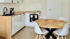 Een moderne keuken met witte kasten, een houten aanrecht en een eethoek met een ronde tafel en witte stoelen.